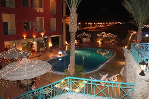 A pool area with a curved design, surrounded by lounge chairs and umbrellas. There are palm trees and a staircase leading to an upper level. - Sun & Sea Hotel and Aqua Park - Hurghada (Hurghada)