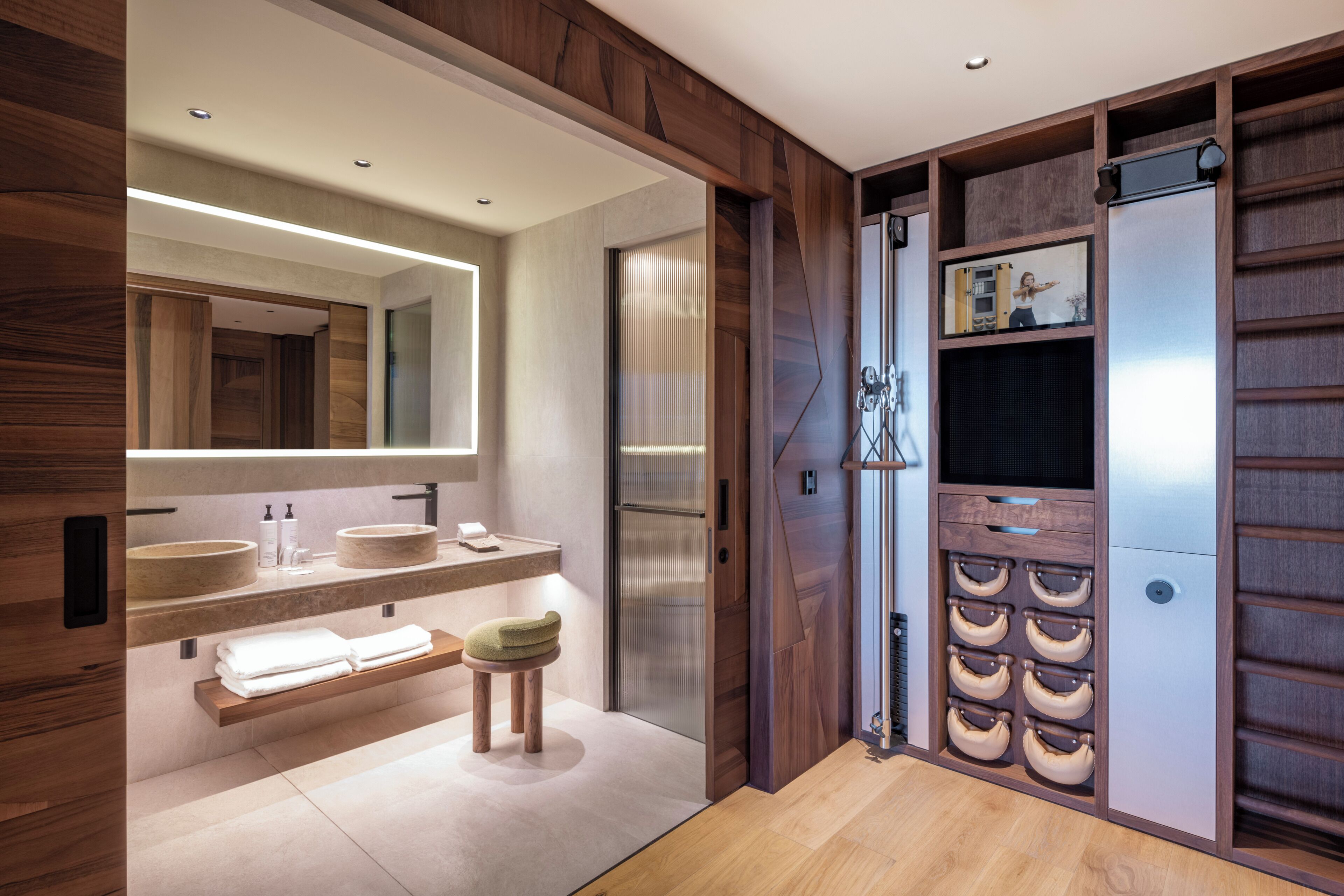 A modern bathroom with wooden paneling, a large mirror, two sinks, a towel rack, and a built-in storage unit.