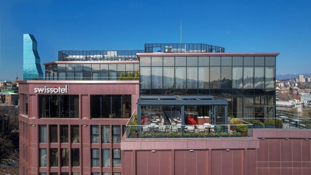 A modern hotel with a glass facade, outdoor seating area, and a view of the cityscape. - Swissôtel Tbilisi (Tbilisi)