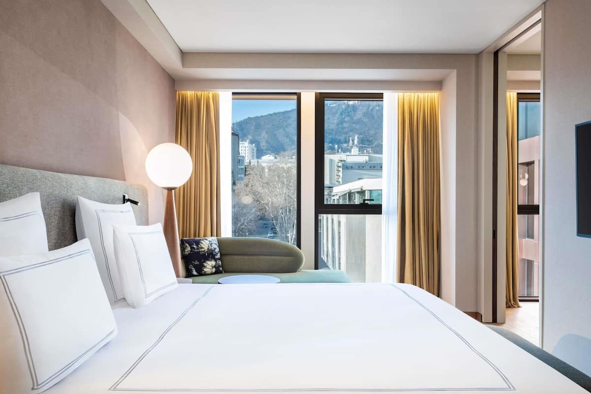A hotel room with a large bed, a view of a cityscape, and a modern design.
