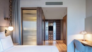 A modern hotel room with a large bed, a desk, and a chair. There is a door leading to a bathroom and a hallway. - Swissôtel Tbilisi (Tbilisi)