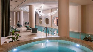 A modern indoor pool area with a clear view of the pool, lounge chairs, and a seating area with a view of the pool. - Swissôtel Tbilisi (Tbilisi)