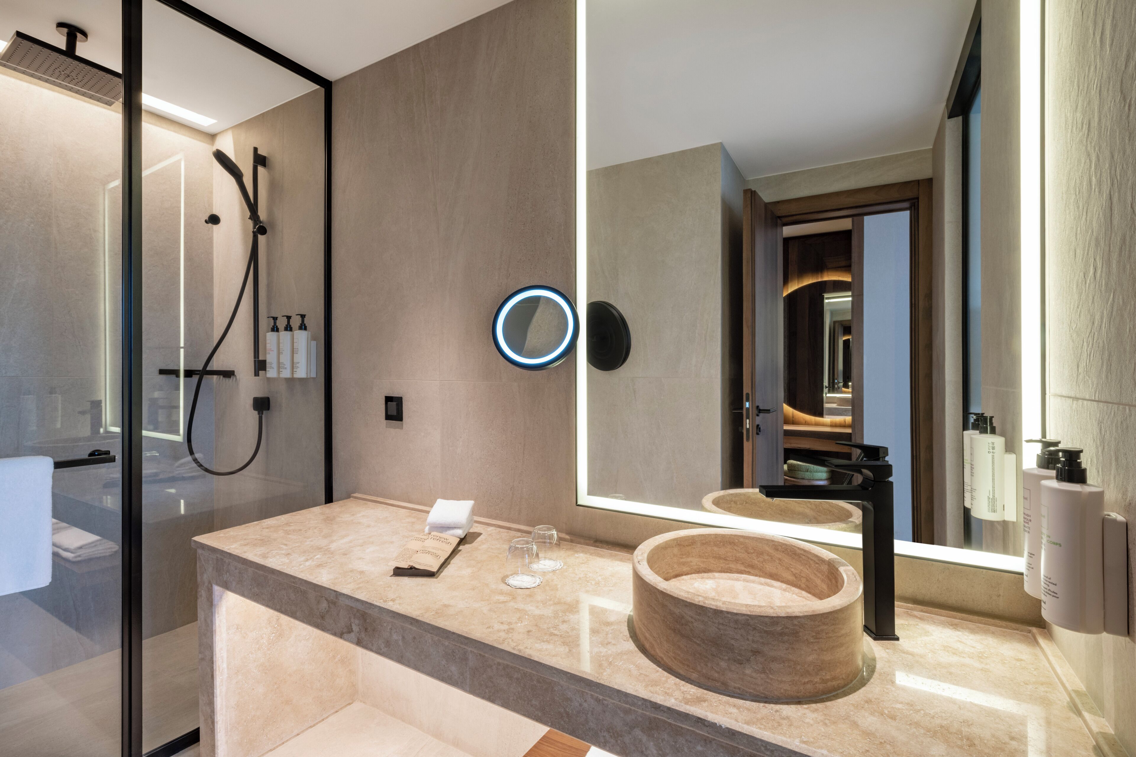 A modern bathroom with a glass-enclosed shower, a large mirror, a marble countertop, and a wooden basin.