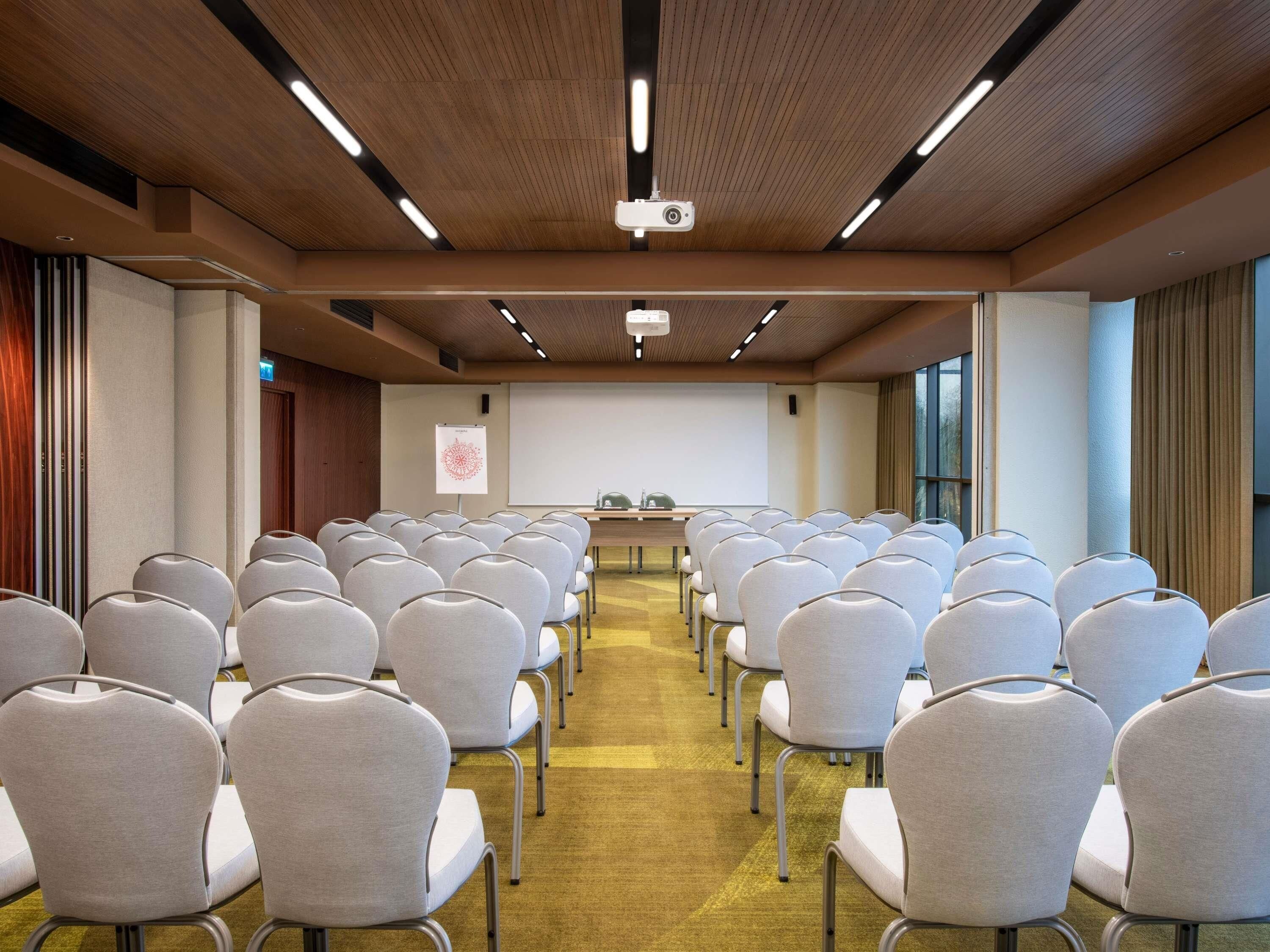 A conference room with rows of chairs, a projector, a whiteboard, and a presentation screen.