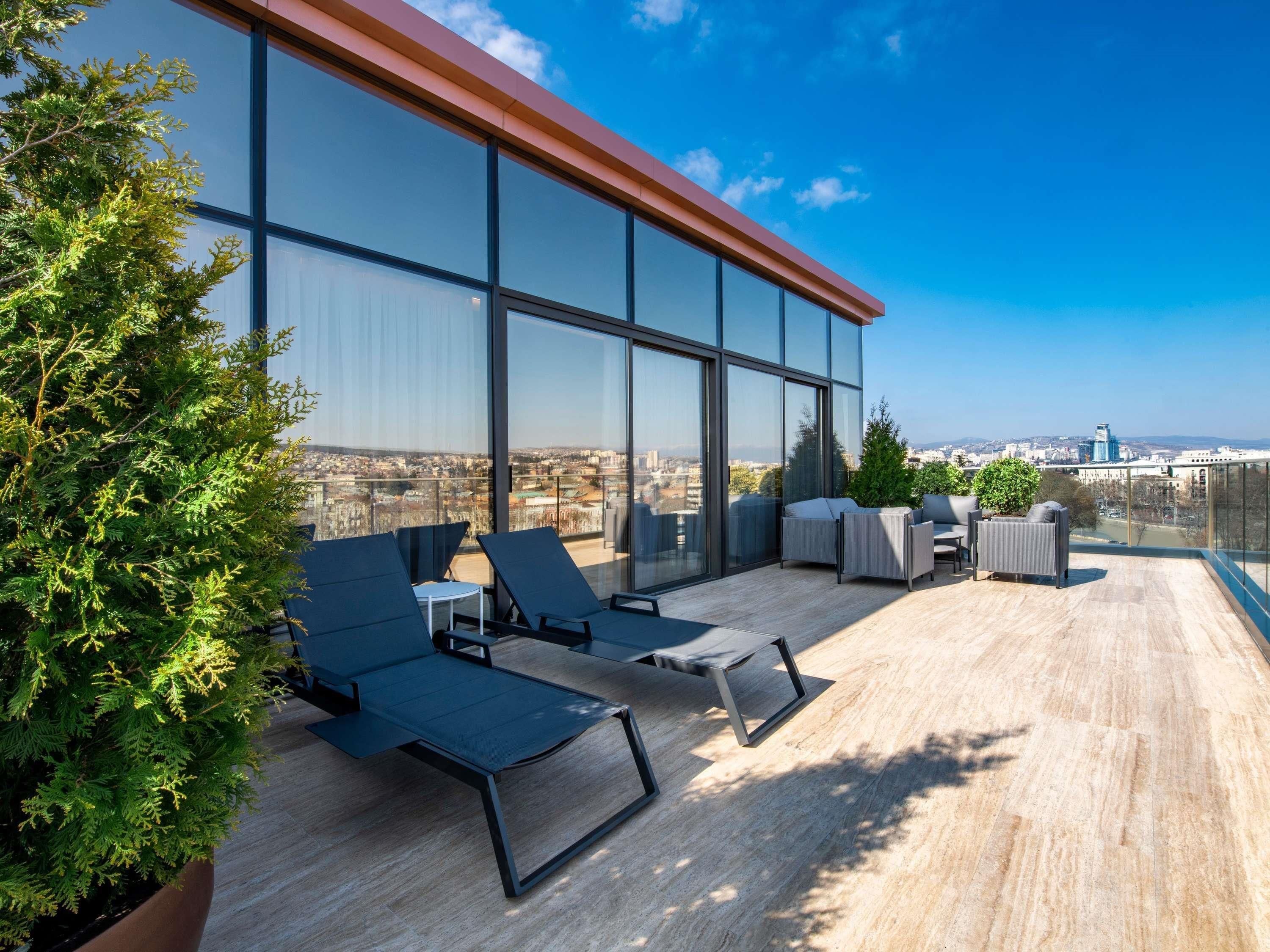 Terraço no telhado com assentos, vista da cidade e um edifício de vidro grande.