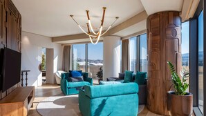 A modern living room with a large TV, teal sofas, a unique ceiling light, and a large window with a city view. - Swissôtel Tbilisi (Tbilisi)