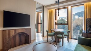 A modern hotel room with a flat-screen TV, a wooden fireplace, a round dining table with chairs, and large windows offering a city view. - Swissôtel Tbilisi (Tbilisi)
