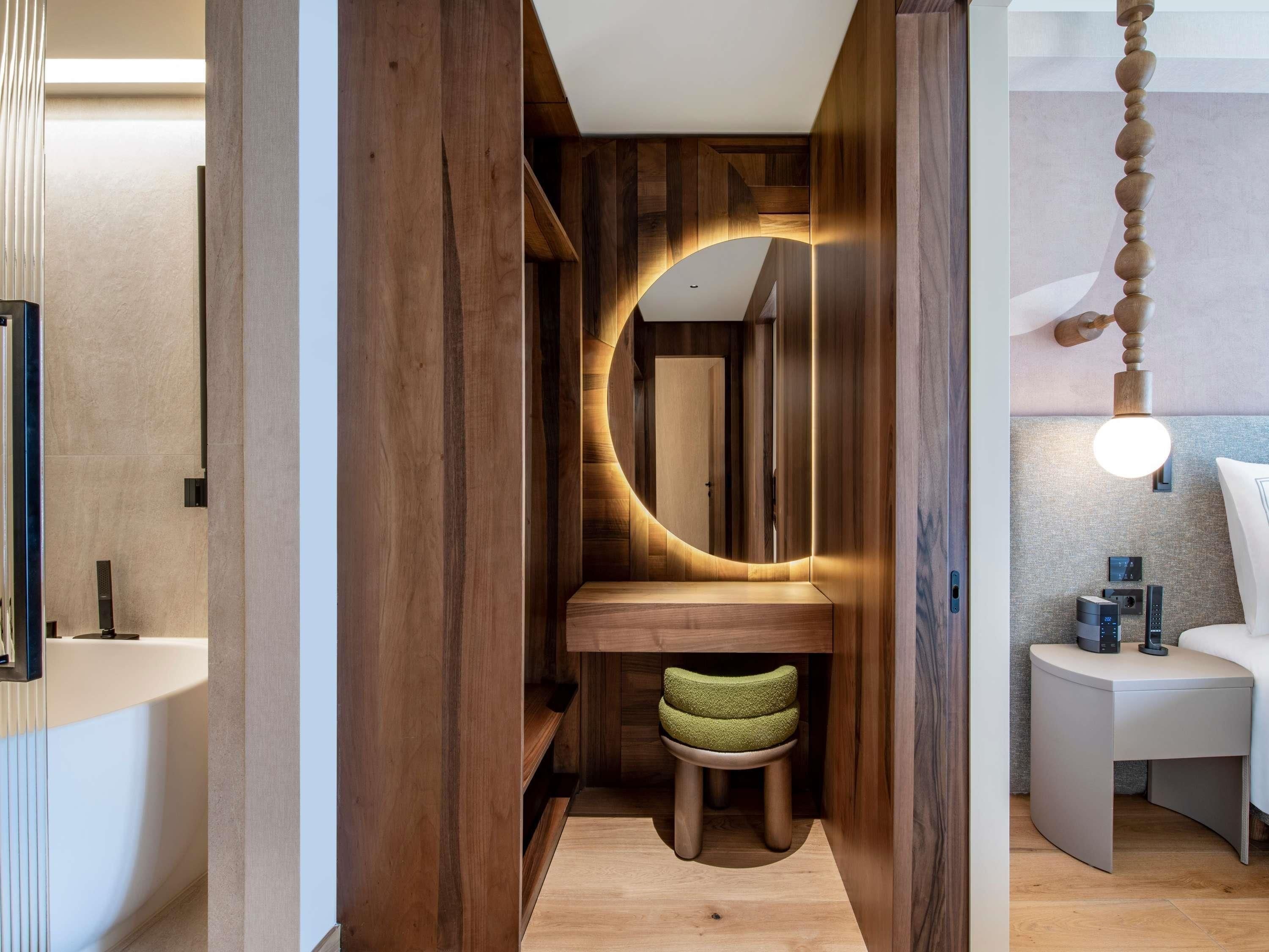 Ein modernes Badezimmer mit einem Holzbadschrank, einem runden Spiegel und einem kleinen Hocker.