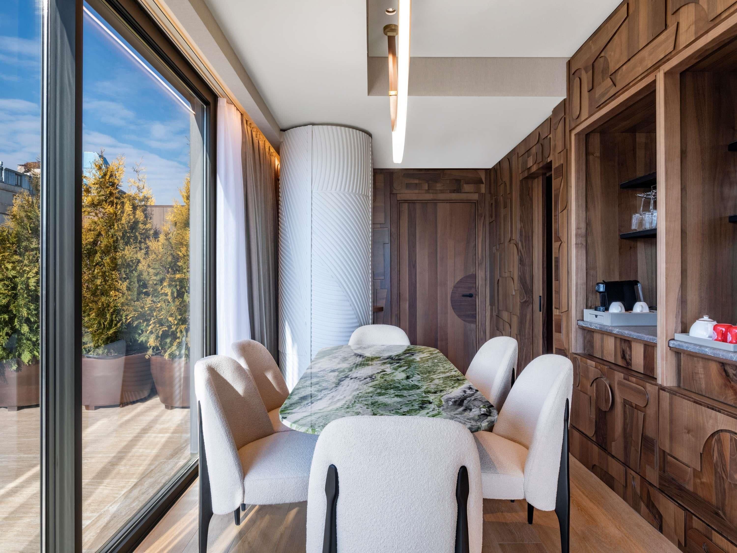 A modern dining area with a round table, four chairs, and a view of trees outside.
