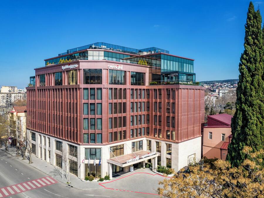 A modern hotel with a red facade, large windows, and a rooftop terrace.