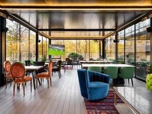 A modern indoor space with a large TV screen, wooden flooring, and a mix of green and brown chairs. - Swissôtel Tbilisi (Tbilisi)