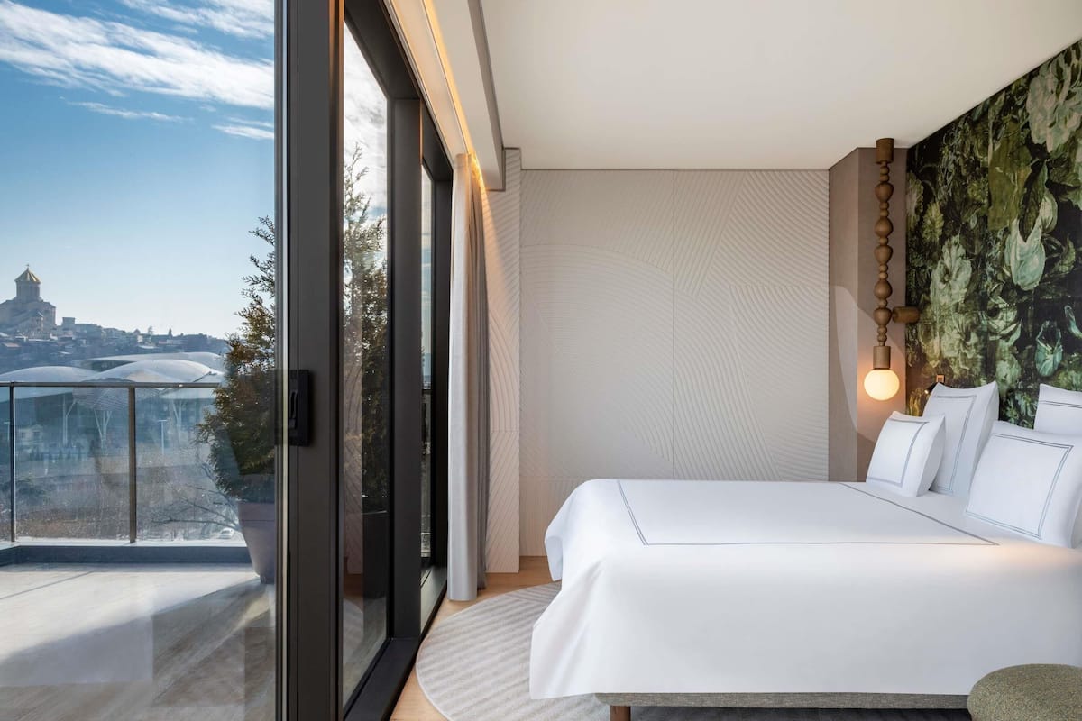 A modern bedroom with a large bed, a view of a cityscape, and a balcony with glass doors.