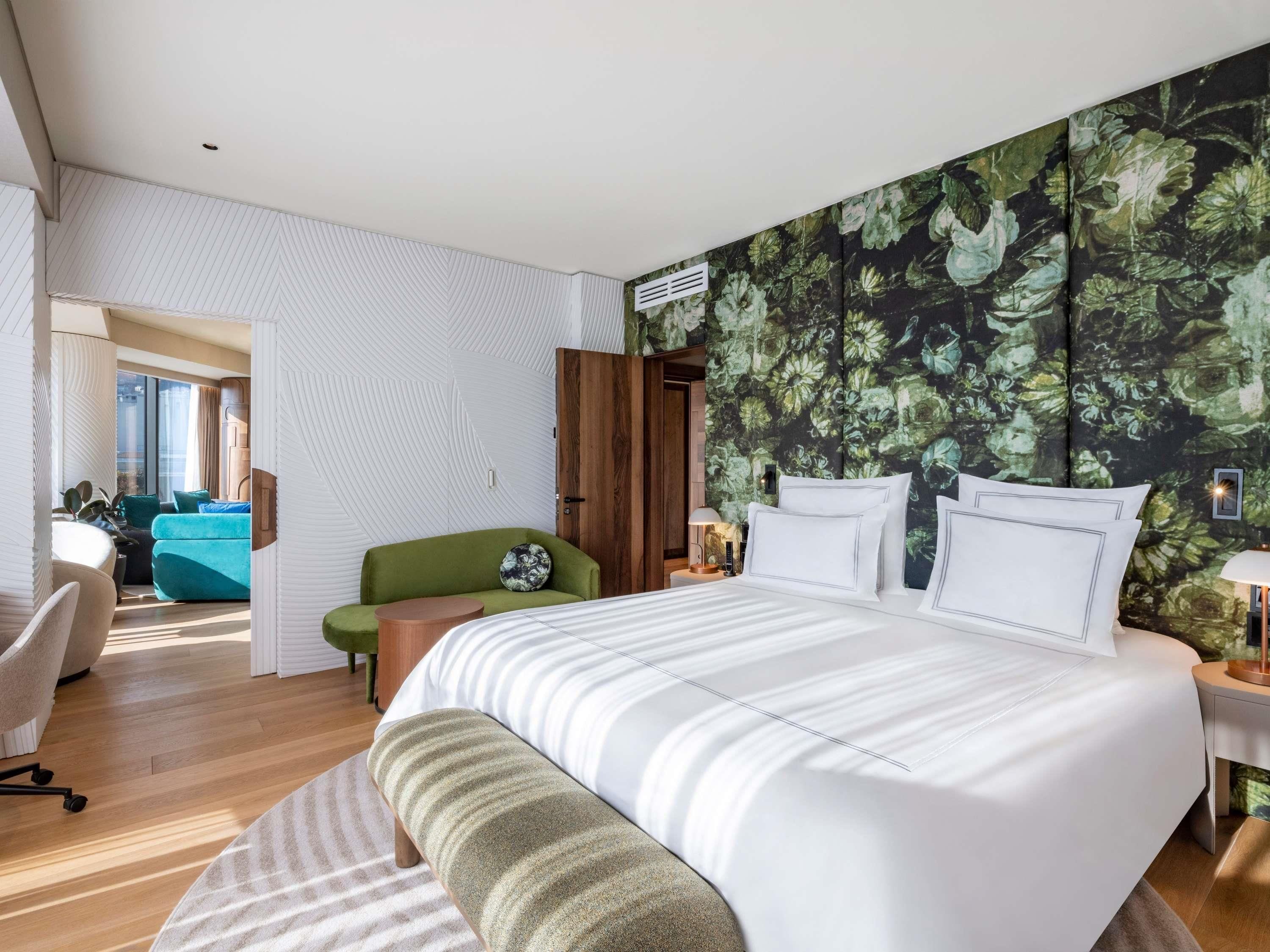 A modern hotel room with a large bed, a green sofa, a desk, and a view of the city.