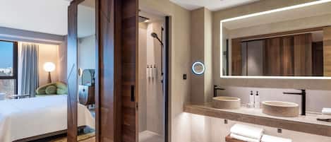 A modern hotel bathroom with a large mirror, a round sink, and a shower area.