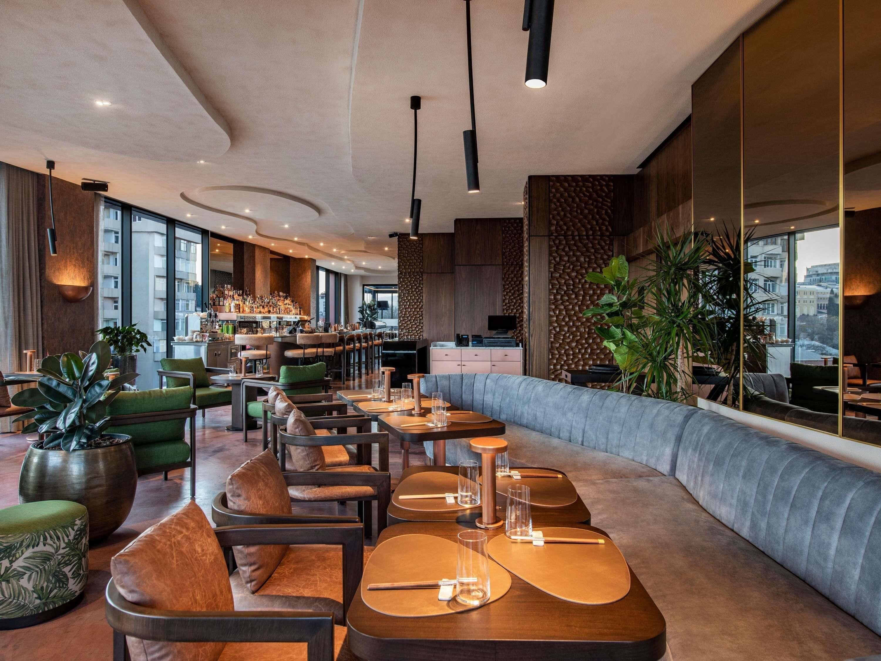 A modern bar/lounge area with seating, a bar counter, and large windows offering city views.