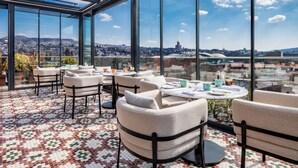 A rooftop terrace with a panoramic city view, furnished with chairs and tables, and a patterned floor. - Swissôtel Tbilisi (Tbilisi)