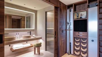 A modern bathroom with wooden accents, a large mirror, two sinks, a vanity, and a towel rack.