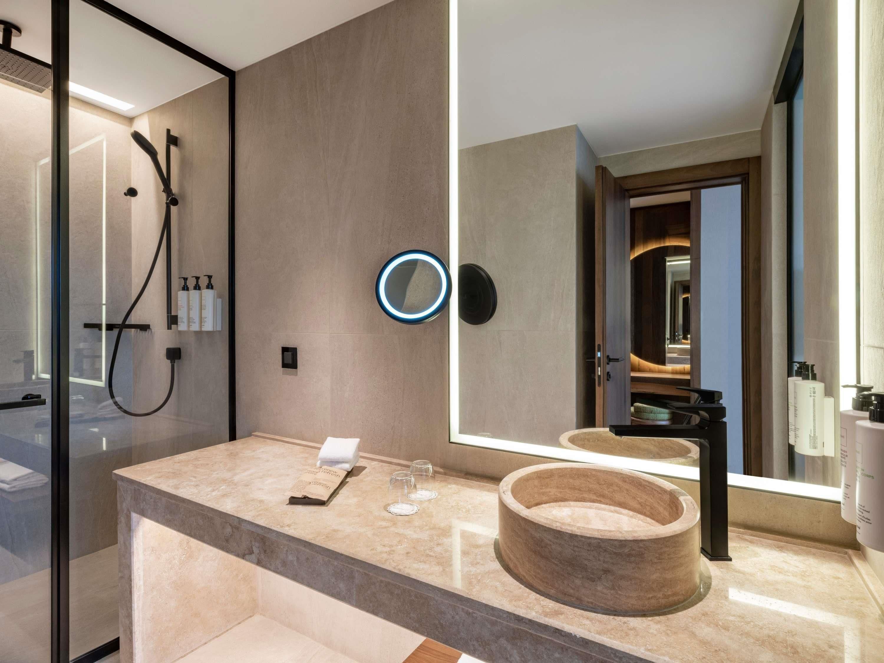 A modern bathroom with a glass shower enclosure, a large mirror, and a wooden basin on the vanity.