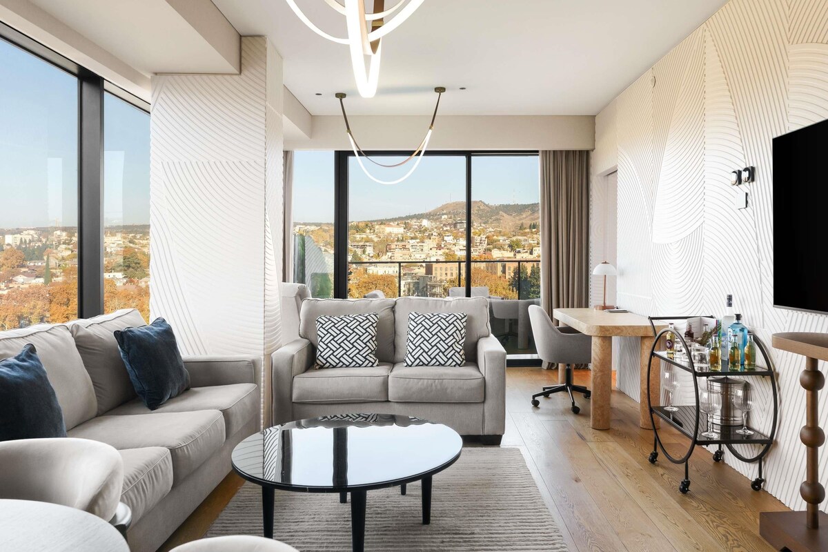 A modern living room with a sofa, a coffee table, a TV, and a view of a cityscape.