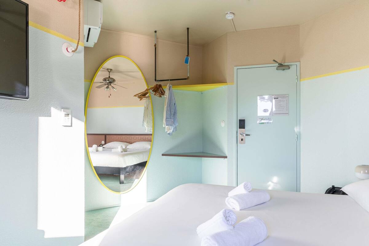 Ein Hotelzimmer mit einem Bett, einem Deckenventilator, einer Tür mit Kartenlese-Schlösser und einer kleinen Ablagefläche.