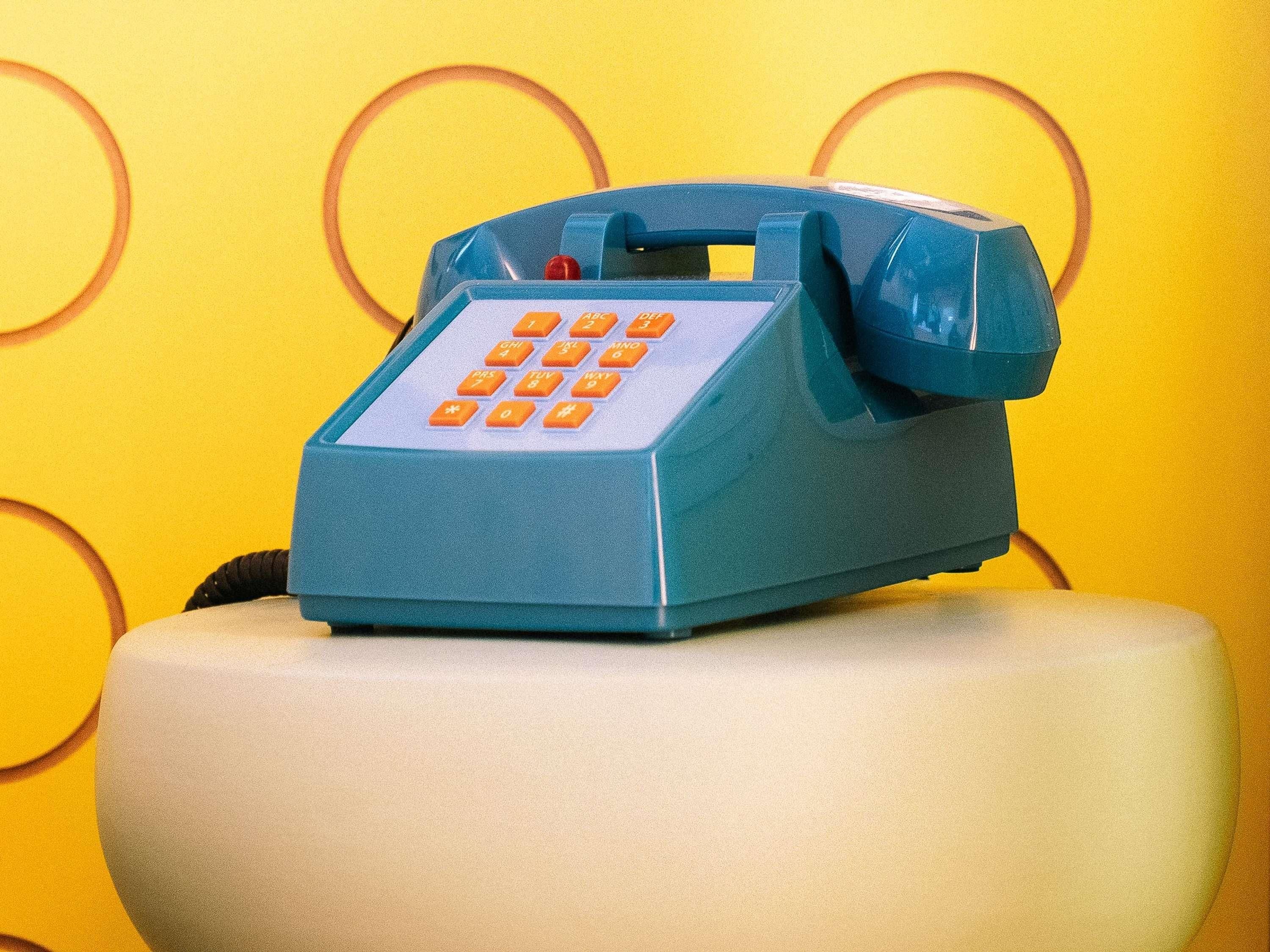 A blue telephone on a white chair against a yellow background with circular patterns.