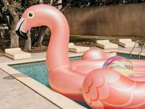 Ein Swimmingpool mit aufblasbaren Flamingo-Schwimmdingen und Liegestühlen.