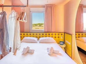 Ein Hotelzimmer mit Bett, zwei Kissen, einem Fenster mit Vorhängen, einem Kleiderhaken und einem Nachttisch mit Telefon.