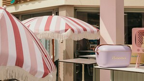 Un petit espace extérieur aménagé avec des parasols à rayures, une table à la surface blanche et un sac violet portant l’inscription « Polarbox », posé sur un support.