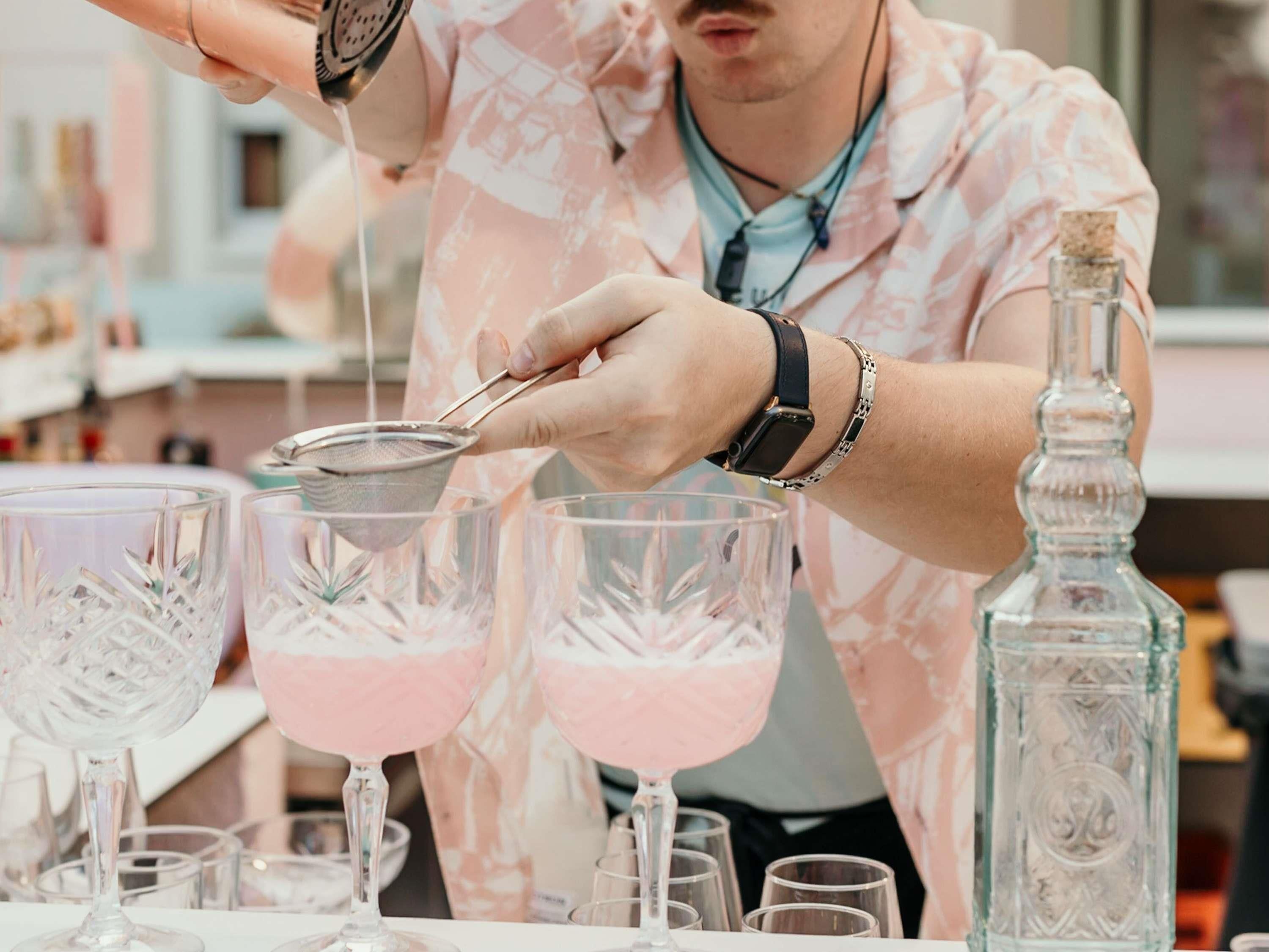 A person pouring a pink liquid into a glass with a strainer.