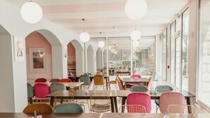 Un espace repas avec des tables et des chaises, de grandes fenêtres et des luminaires suspendus.
