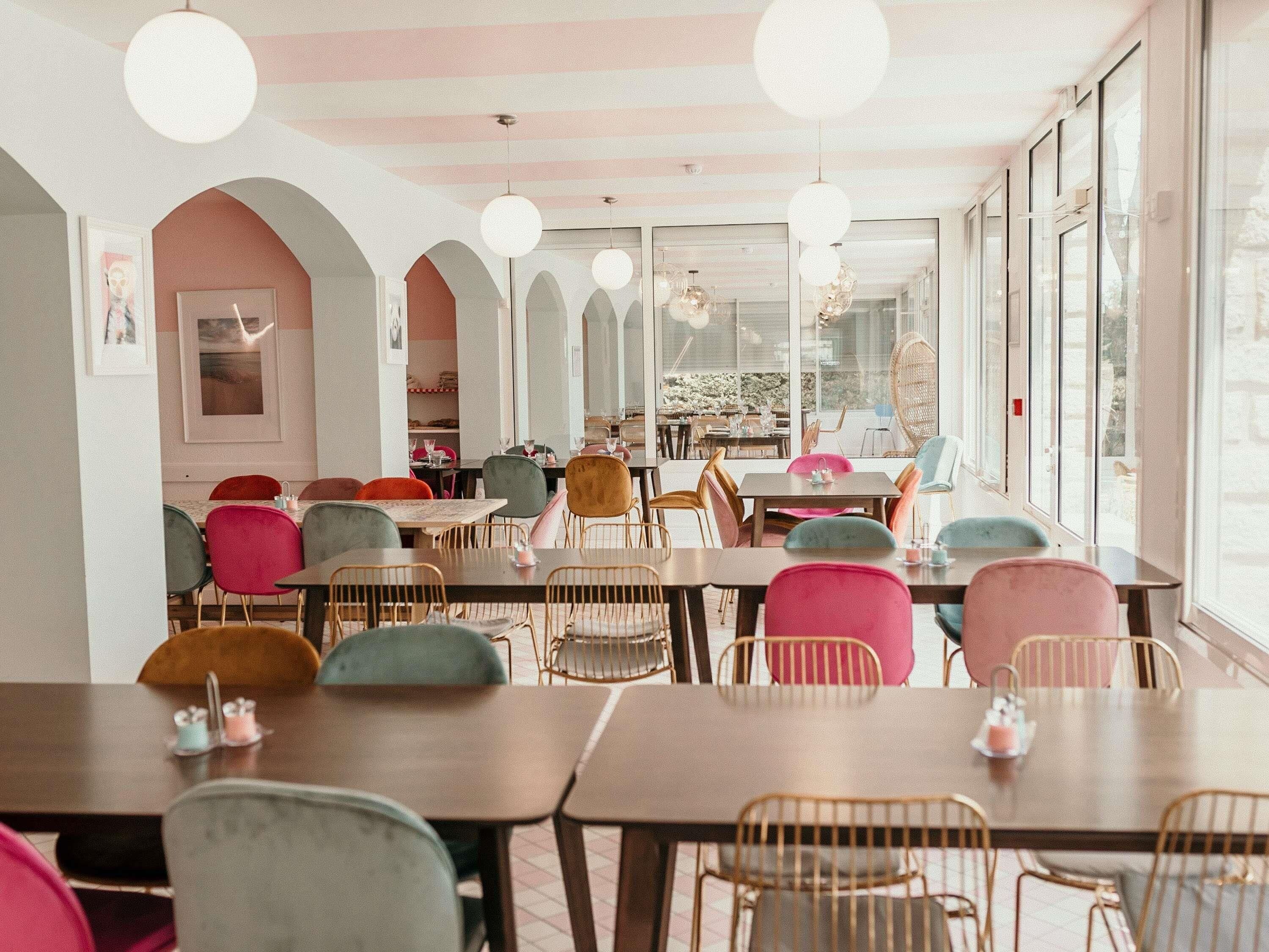 Un comedor con mesas y sillas, ventanas amplias y lámparas colgantes.