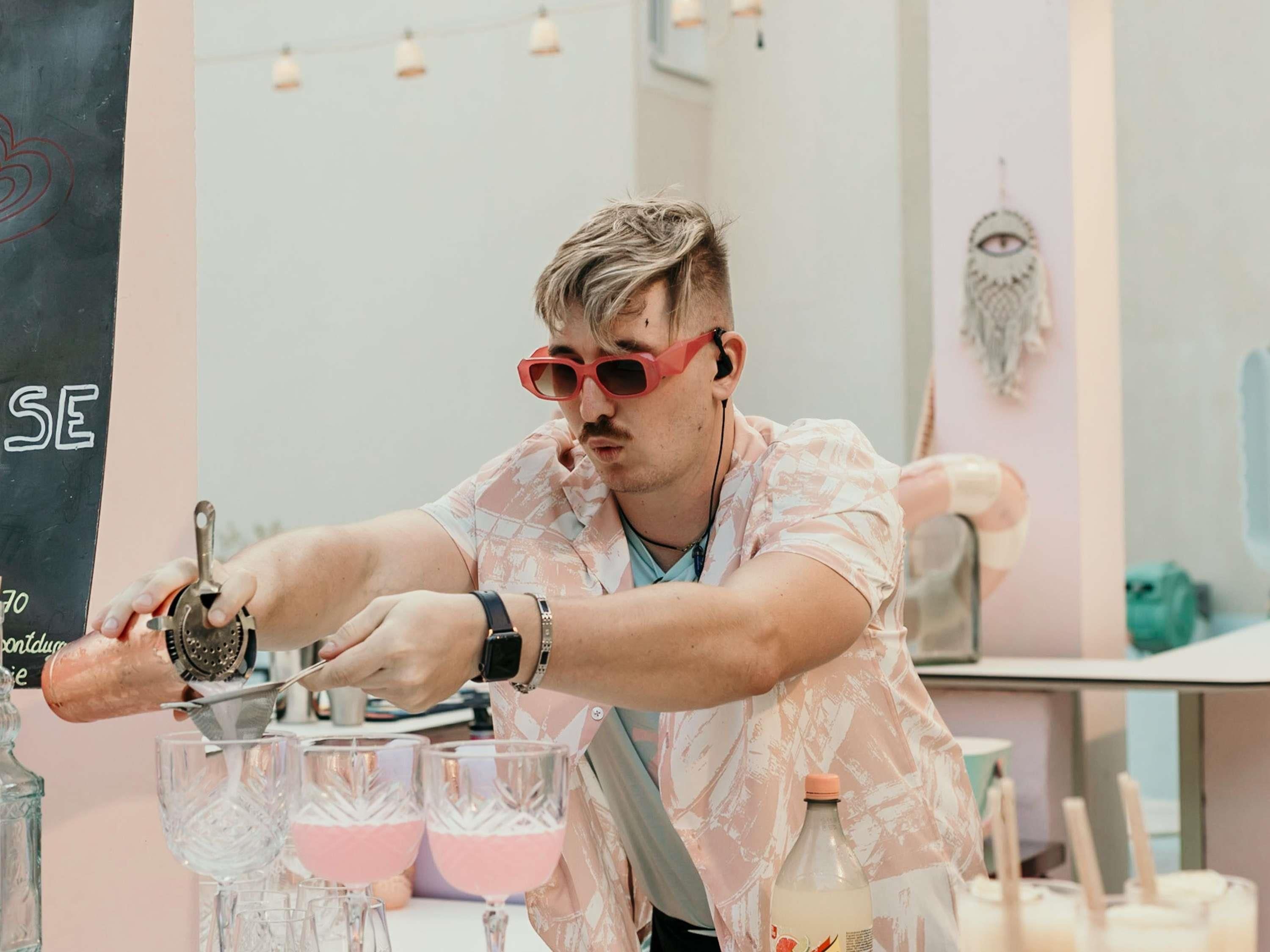 Una persona preparando bebidas en una barra, con vasos y una botella.
