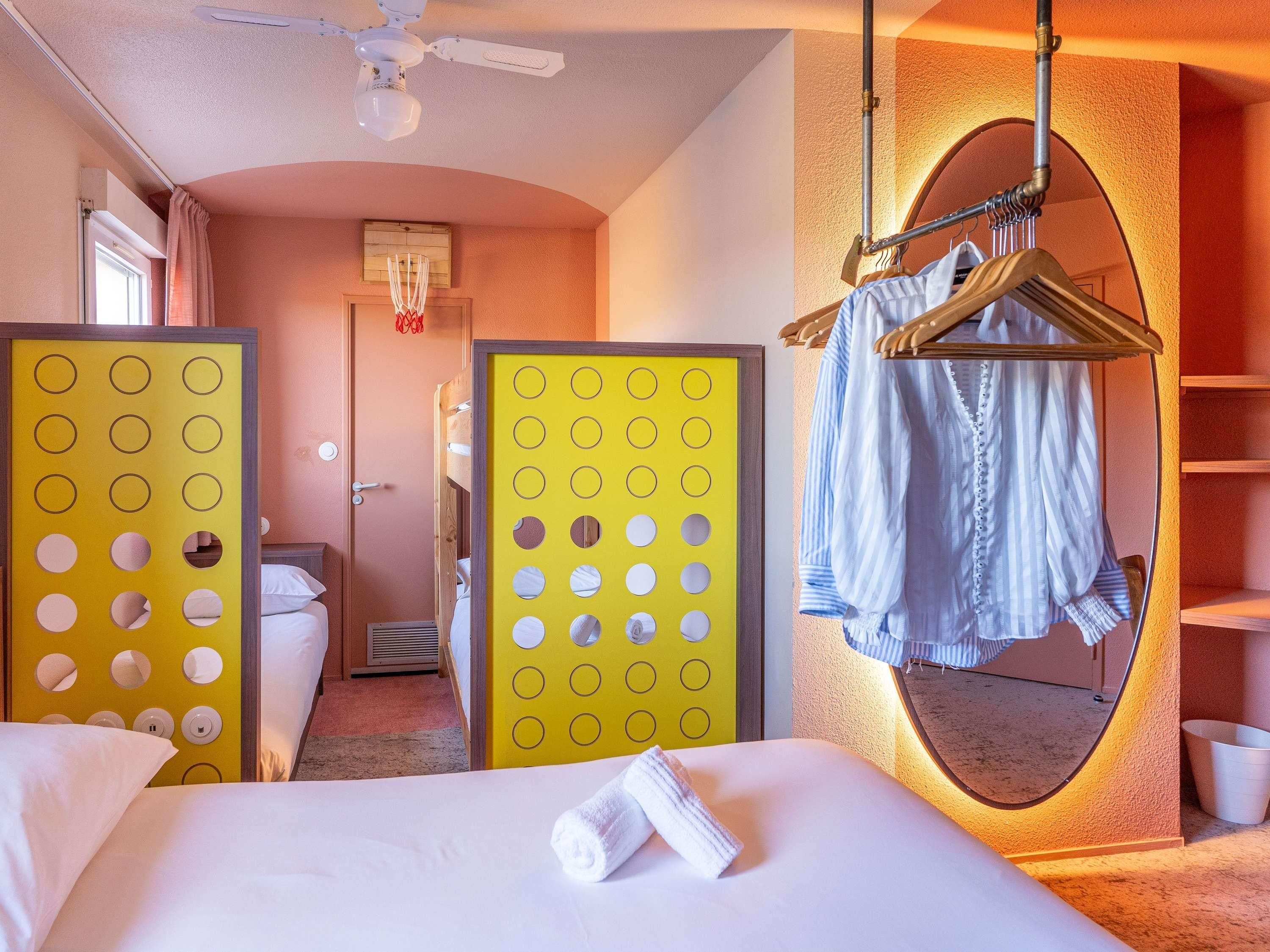 Habitación de hotel con cama, espejo, perchero y un separador con círculos.