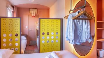 Habitación de hotel con cama, espejo, perchero y un separador con círculos.