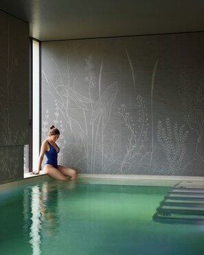 A person sitting by a pool with a wall featuring plant designs. - Domaine de la Reine Margot Paris-Issy - MGallery Collection (Issy-les-Moulineaux)