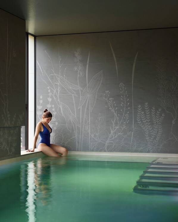A person sitting by a pool with a wall featuring plant designs. - Domaine de la Reine Margot Paris-Issy - MGallery Collection (Issy-les-Moulineaux)