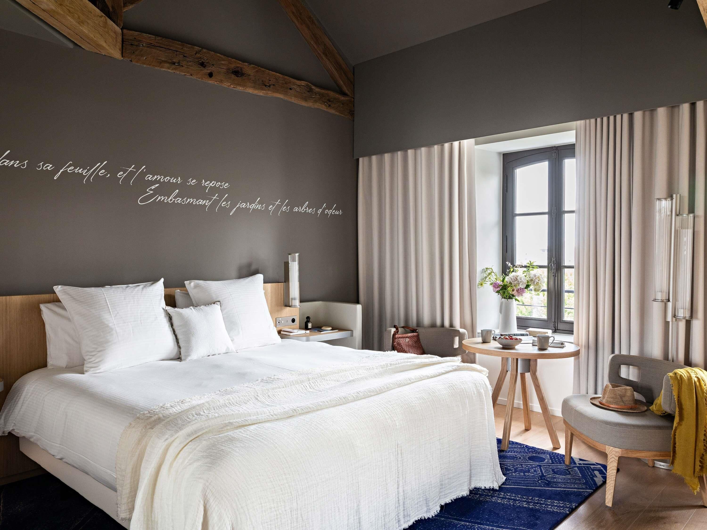 A modern bedroom with a large bed, a bedside table, a chair, and a window with curtains.