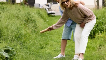 A person in a beige sweater and white pants holding a stick, standing in a grassy area with a building in the background.