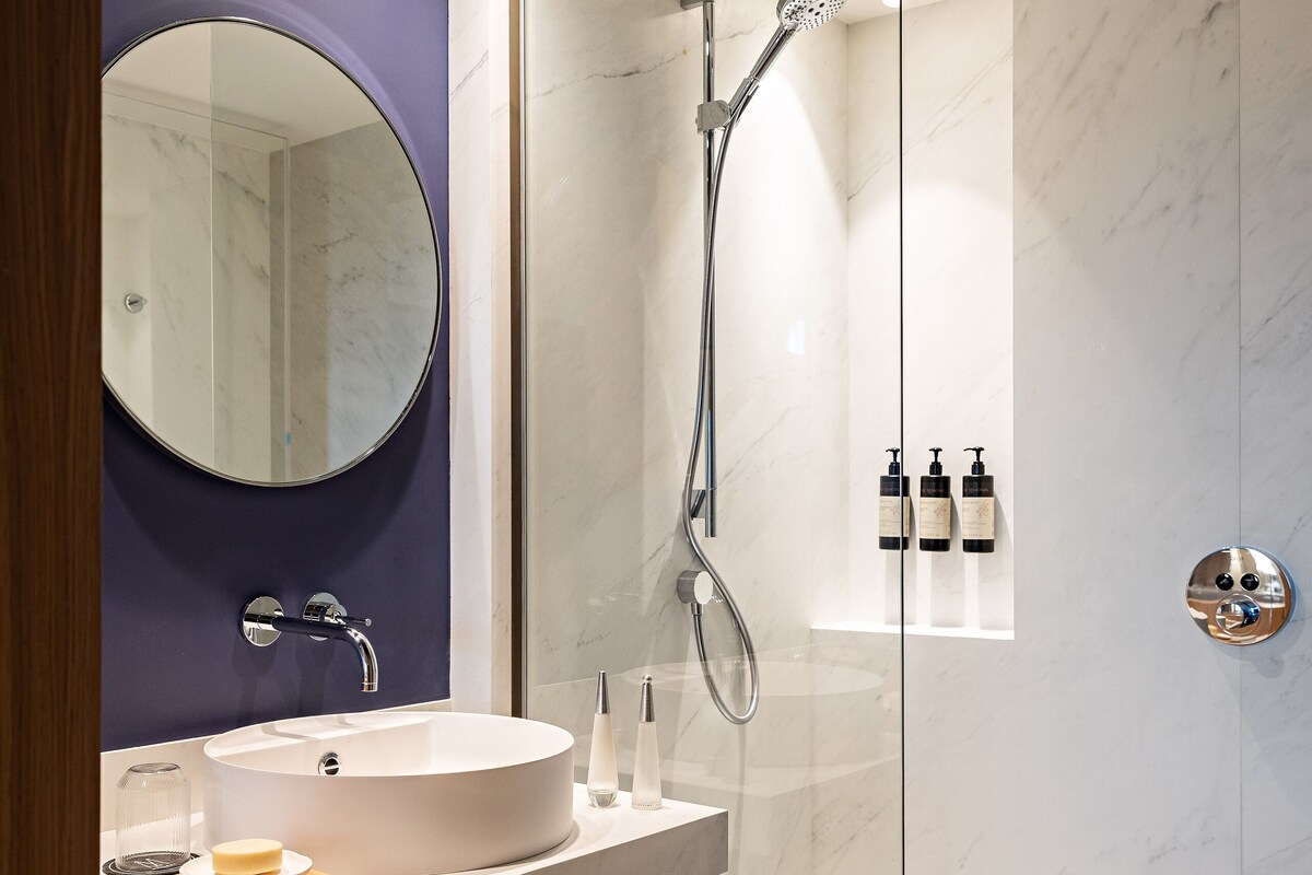 A modern bathroom with a glass-enclosed shower, a round mirror, and a wooden vanity.