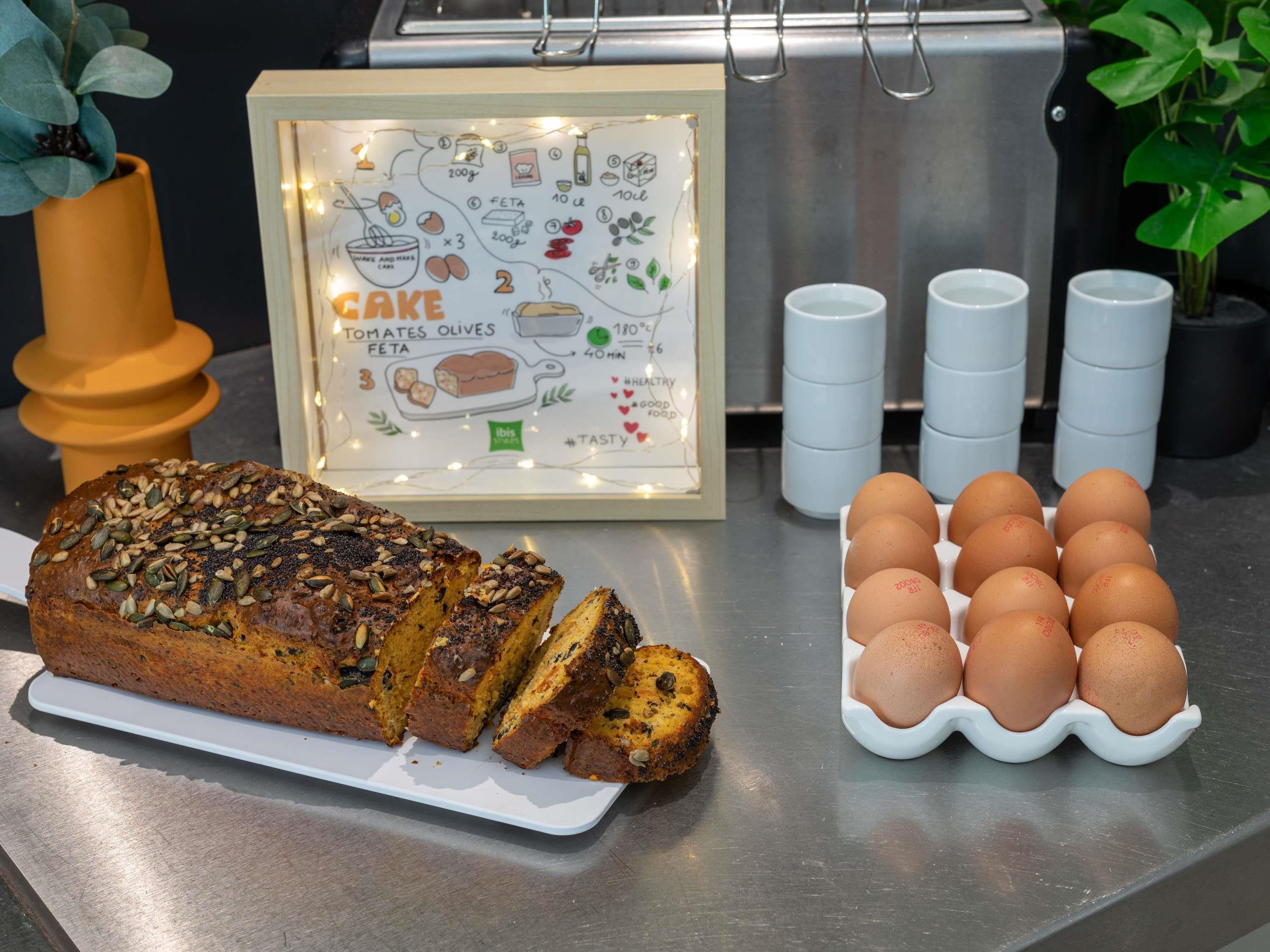 A loaf of seeded bread on a white plate, a carton of eggs, and a framed recipe card with illustrations of food items.