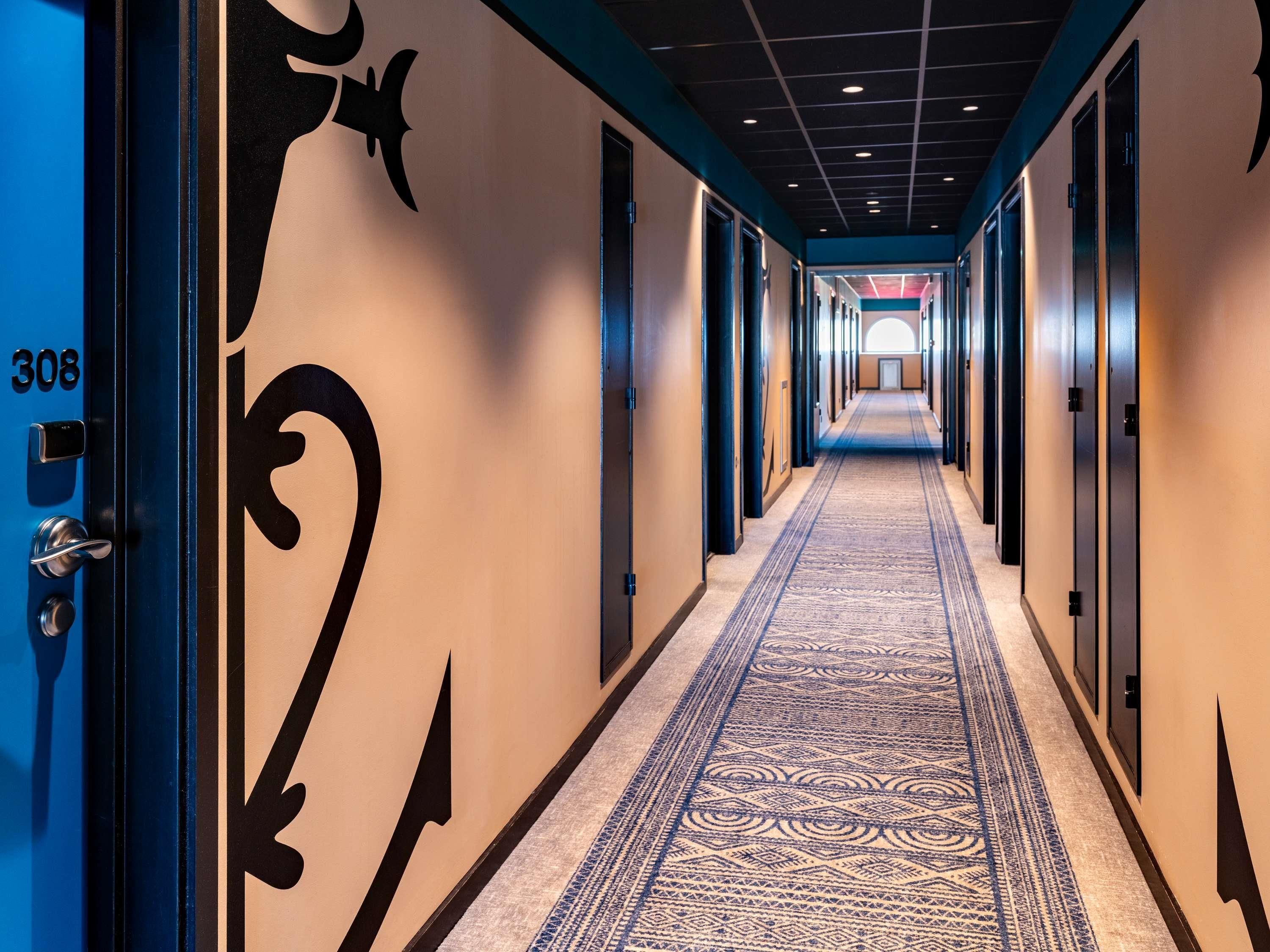 Un couloir d’hôtel avec un sol recouvert de moquette, des portes des deux côtés et le numéro « 308 » sur la porte de gauche.