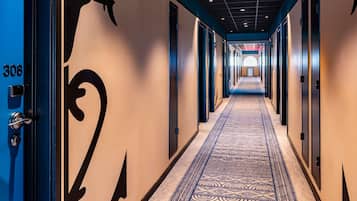 A hotel hallway with a carpeted floor, doors on both sides, and a number '308' on the left door.