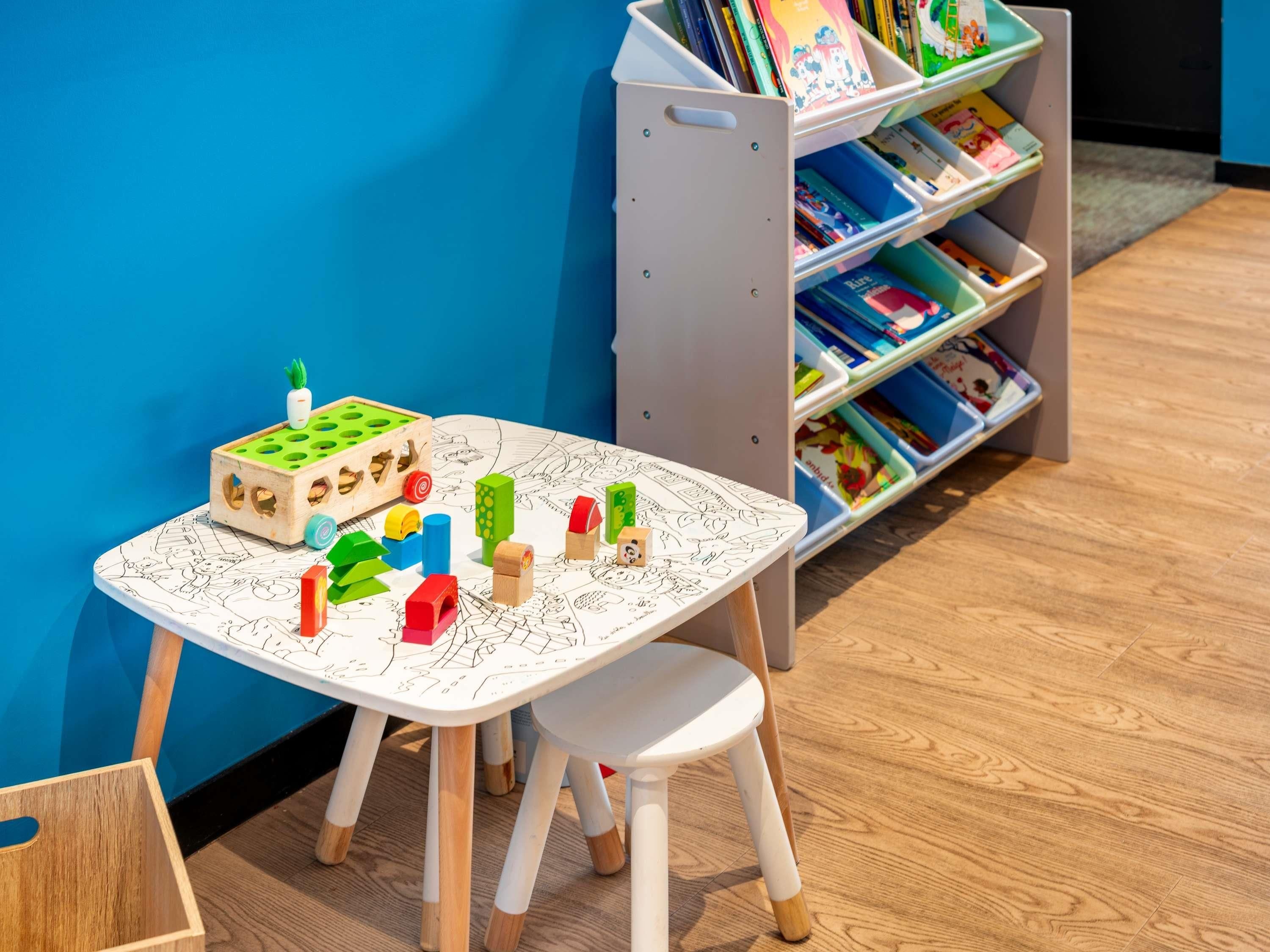 Ein Kinderspielbereich mit Tisch und Stühlen, umgeben von einem Bücherregal voller Bücher.