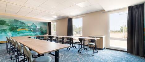 A conference room with a long table, chairs, a painting on the wall, and large windows.