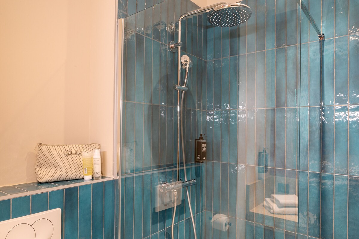 A bathroom with a glass-enclosed shower, a towel rack, and toiletries on a shelf.