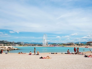 A beach with people sunbathing and swimming, a Ferris wheel in the background, and a clear sky. - Ibis Styles Miramas - Provence (Miramas)