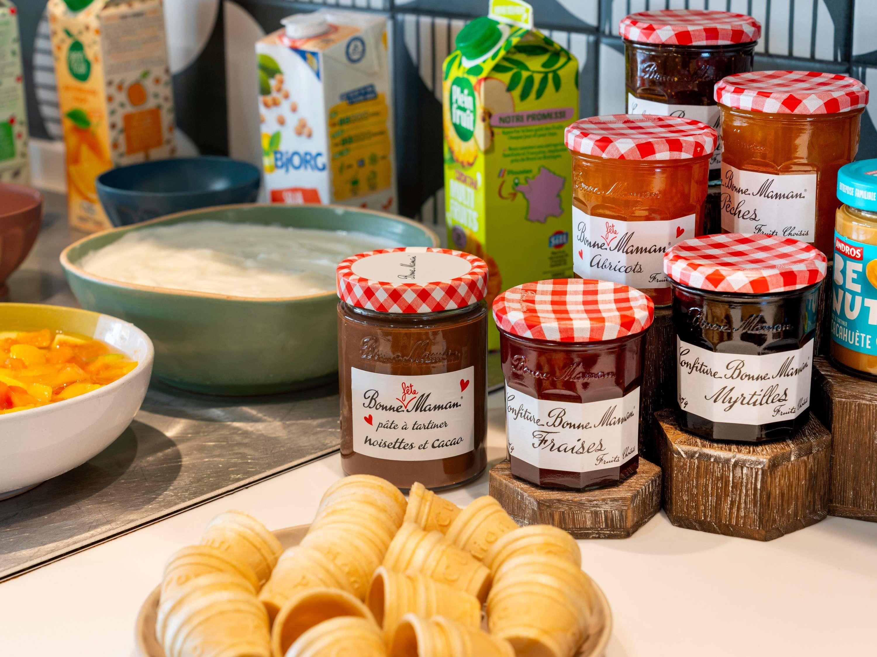 On trouve une variété d’aliments, notamment des pots de miel, des pots de confitures de fruits, un bol de compote de fruits et un bol de crème.
