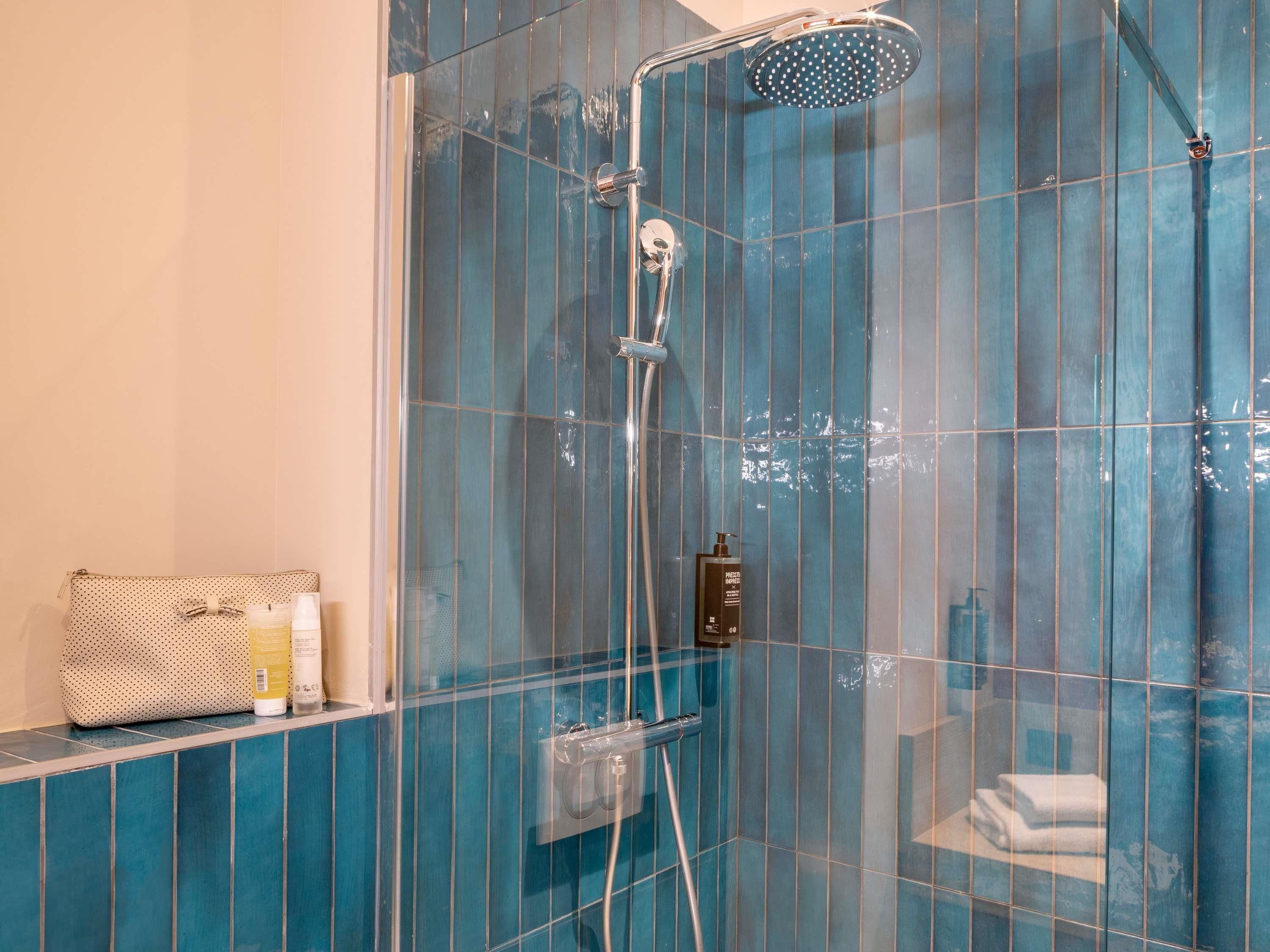 Ducha envuelta en vidrio con cabezal de ducha de mano, toallero y artículos de aseo en un estante.