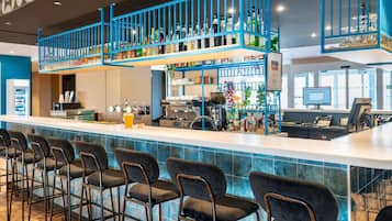 A bar area with multiple seating options, a counter with a beverage dispenser, and a variety of bottles and glasses on shelves.