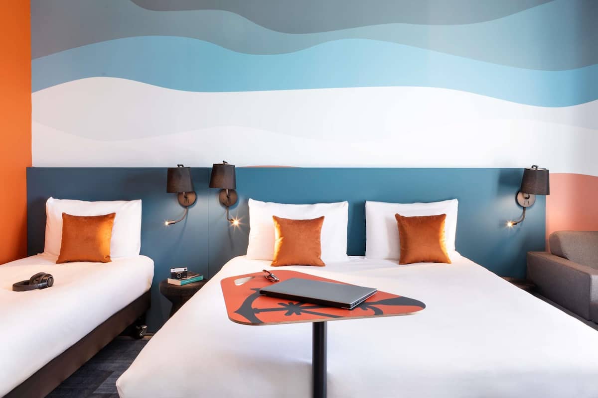 Quarto de hotel com uma cama, duas mesas de cabeceira, uma escrivaninha com um laptop e luminárias fixadas na parede.